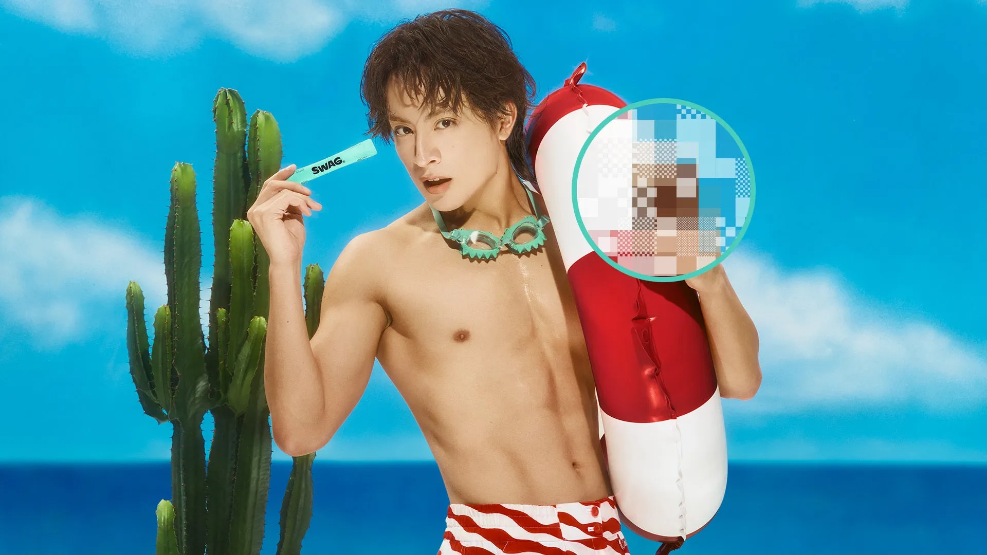 男性が浮き輪を持ち、サングラスをかけ、日差しの下でポーズをとっている画像です。男性は上半身裸で、ビーチパンツを履いています。背景にはサボテンと青い空があります。