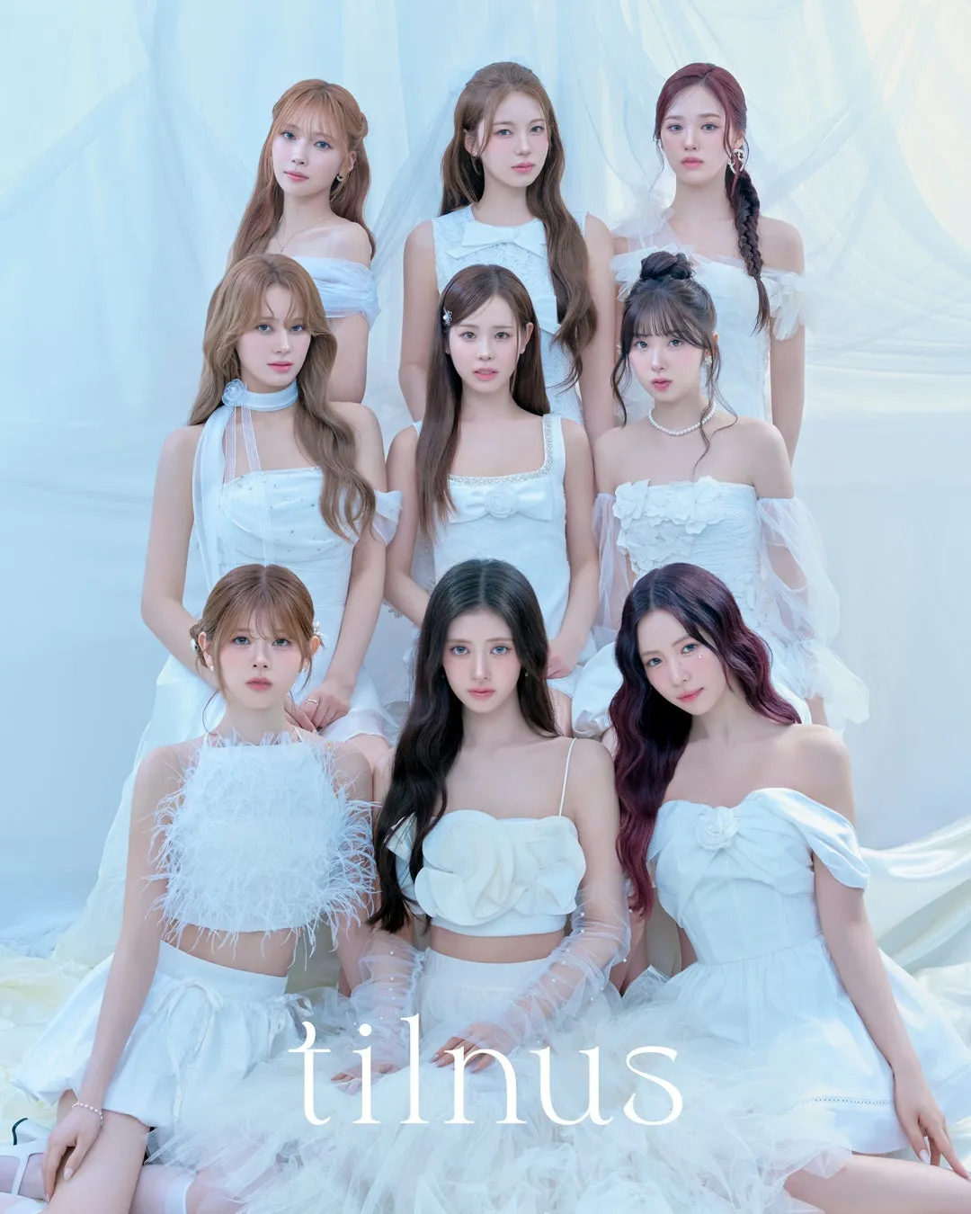 白いドレスを着た9人の女性のグループの写真。彼女たちは白い背景の前に座っています。