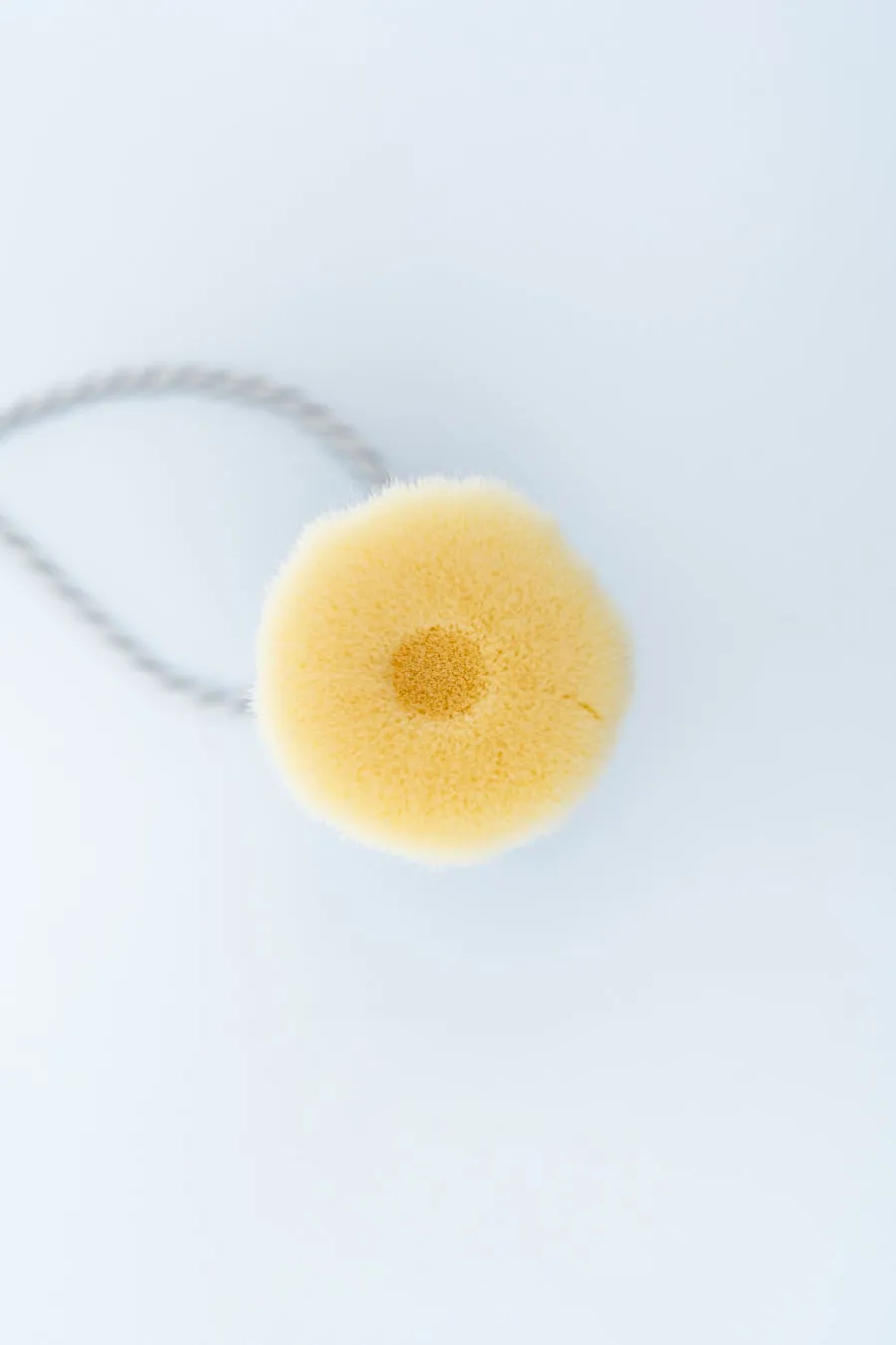 黄色いヘアスタイリングツールが白い背景に置かれています。中央には丸い形状のツールがあり、その中心には濃い黄色の円があります。ツールはひもでつながっています。