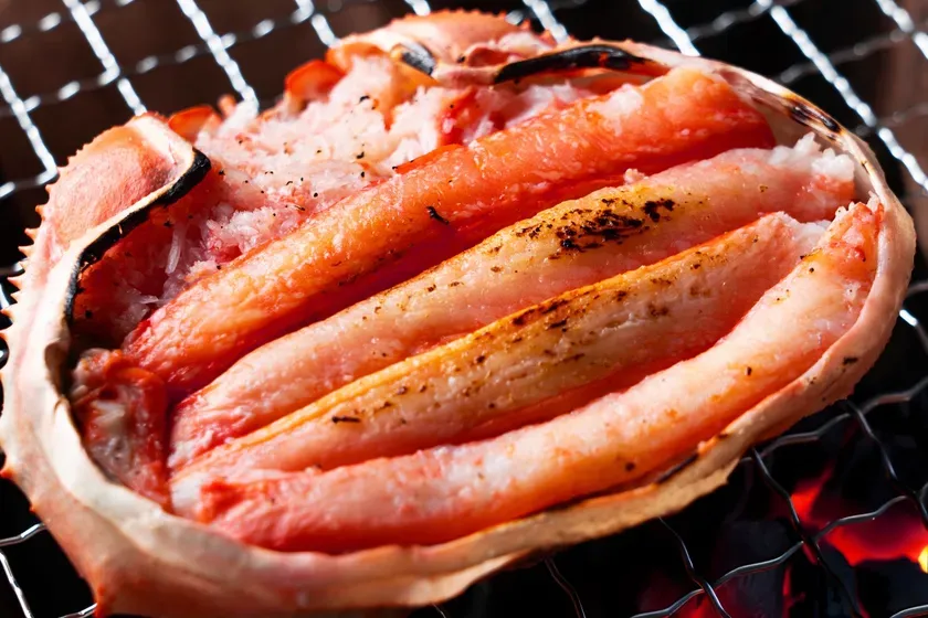 網の上で焼かれたカニの画像です。カニの身は赤く、焼き目がついています。カニの殻が写っています。