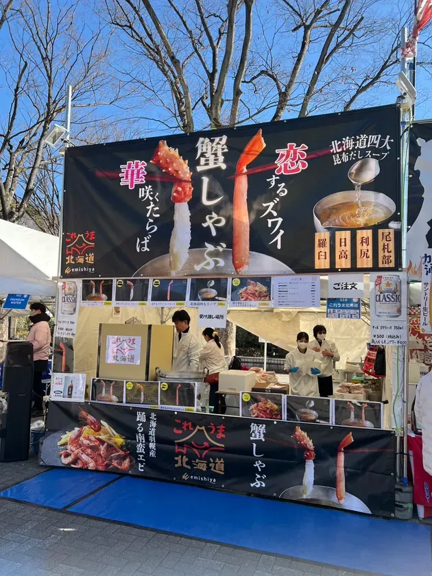 屋台で販売されている蟹しゃぶの画像。看板には「恋するズワイ」の文字と、蟹のイラストが描かれている。店員が調理をしている様子も写っている。