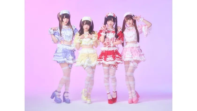 4人の女性がカラフルなコスチュームを着てポーズをとっている写真。ピンク色の背景に、それぞれの衣装が異なる色合いで、統一感がある。