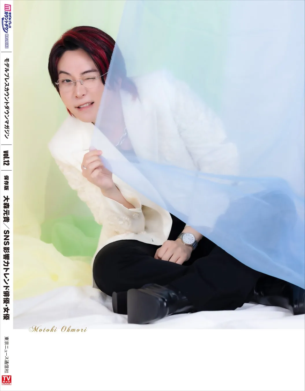 大森元貴が写った雑誌の表紙。水色の布の前に座り、ウィンクをしている。