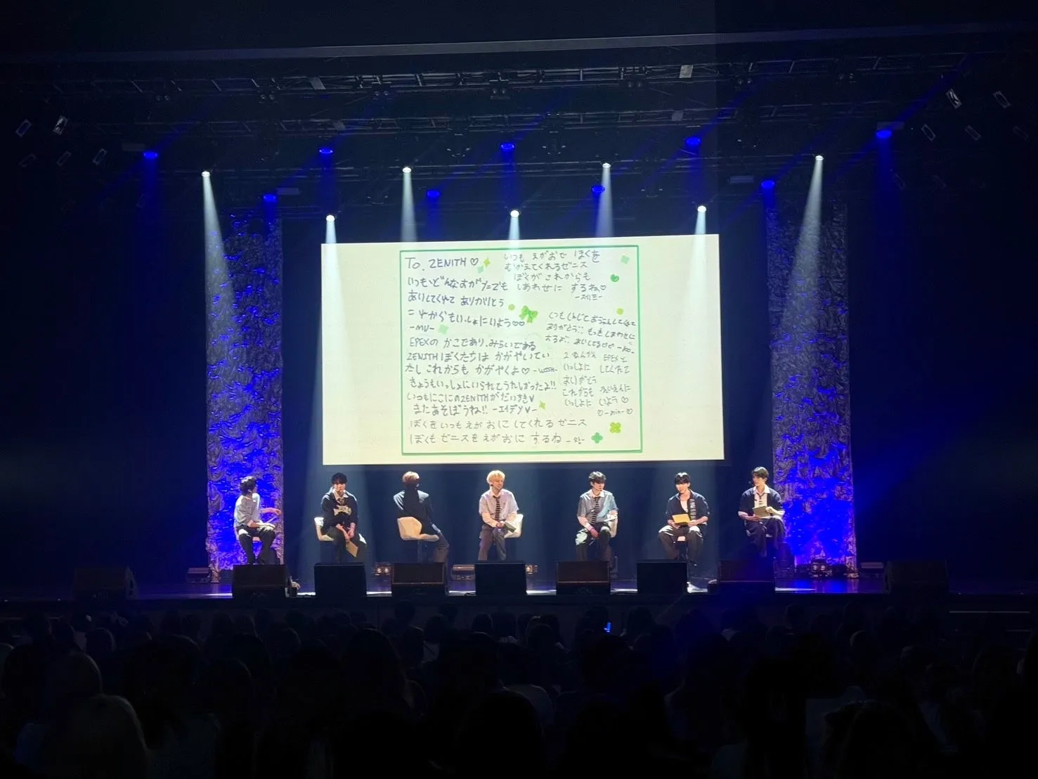 ステージ上で観客を前に、ファンからのメッセージボードを持って座るEPEXのメンバー。