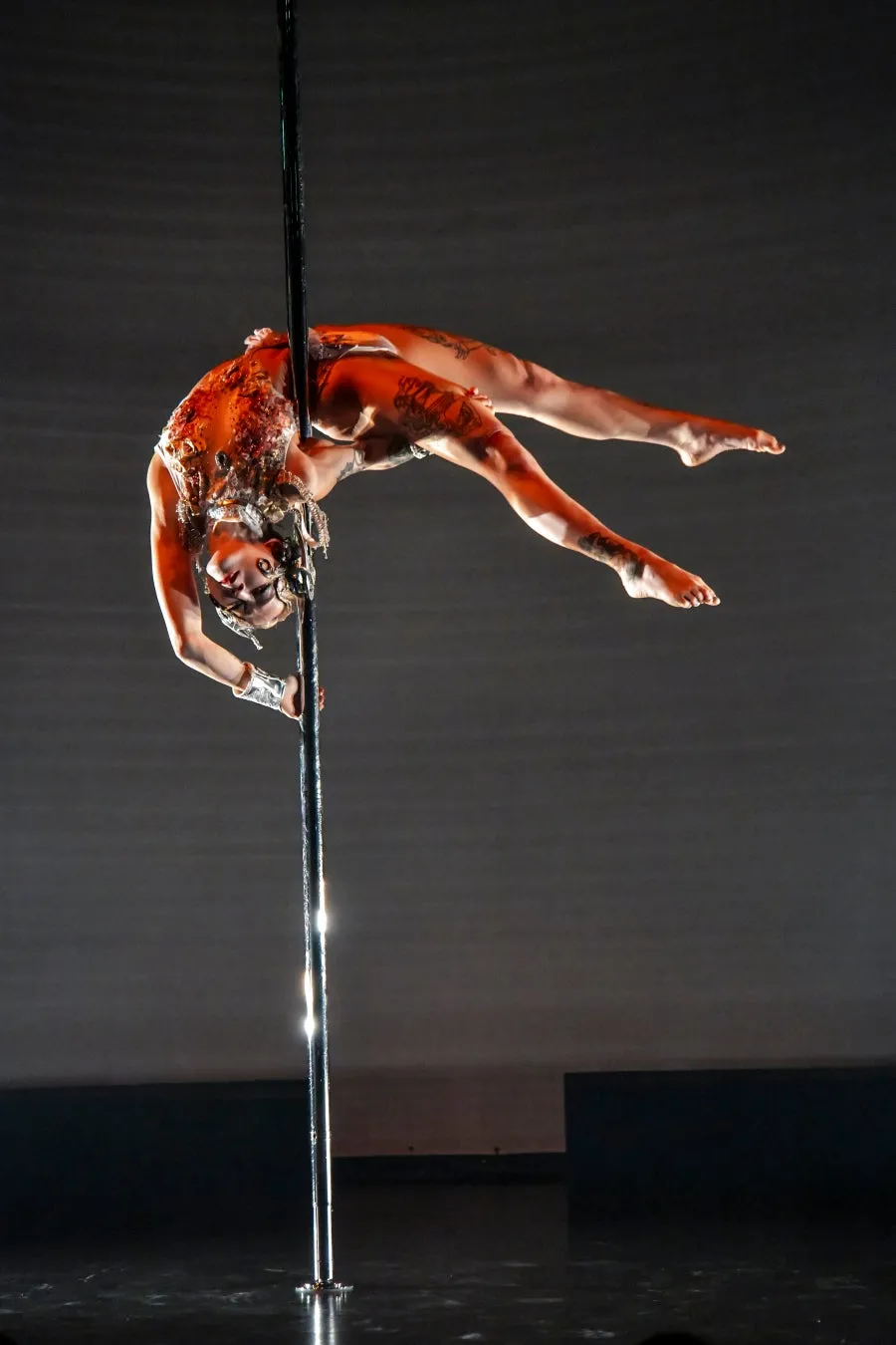 ポールダンスをしている女性。逆さまになって体を支え、アクロバティックなポーズをとっている。