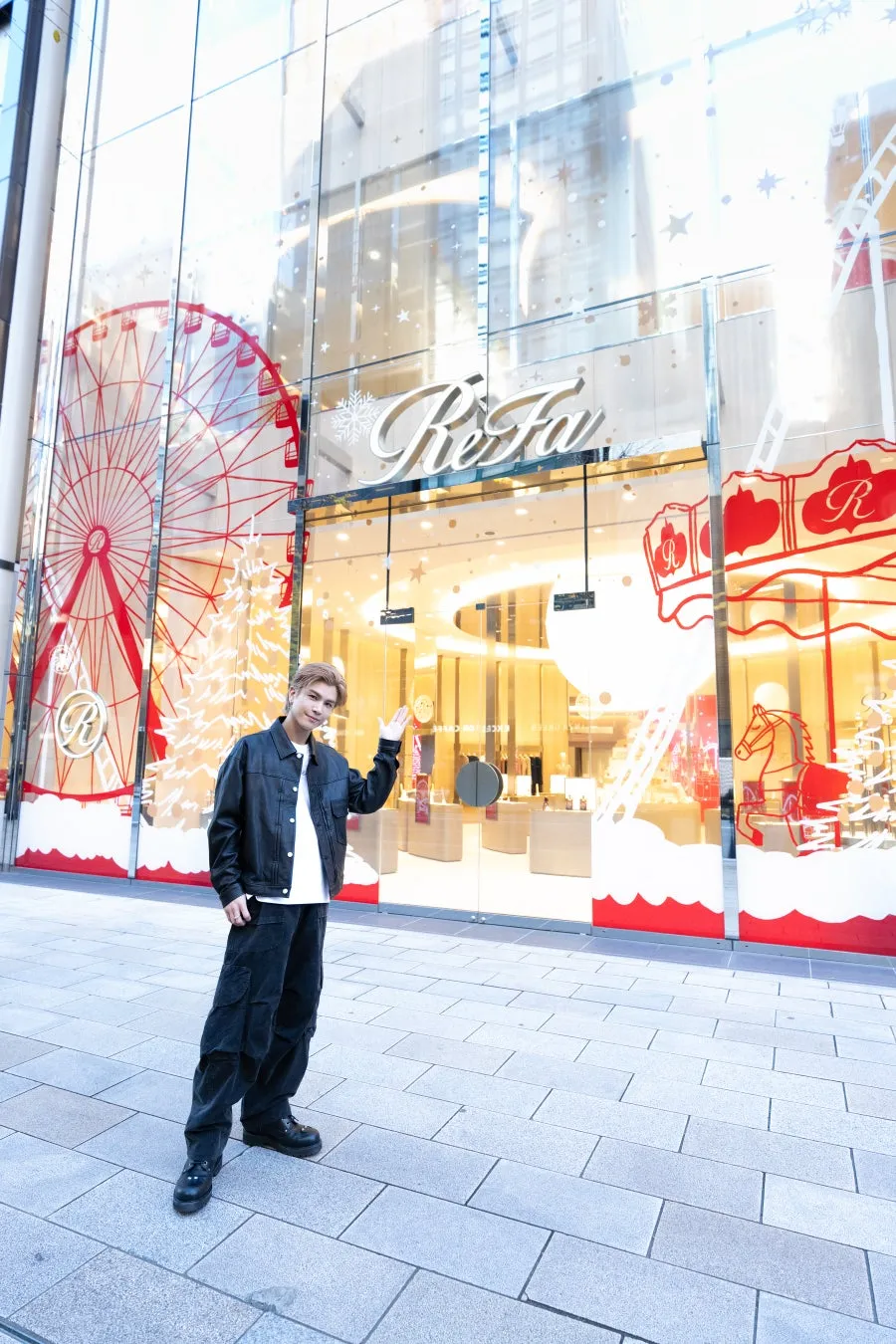 男性がReFaの店舗の前でポーズをとっている写真。店舗はクリスマスの装飾が施されており、観覧車やメリーゴーランドのイラストが描かれている。