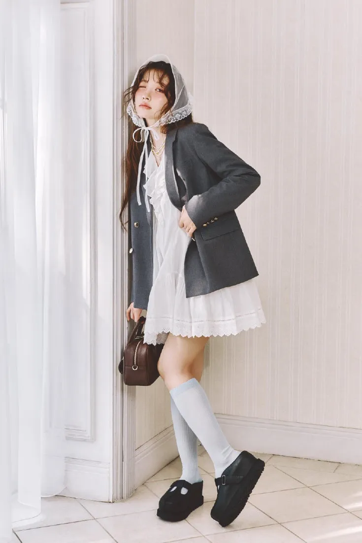 女性が白いドレスとグレーのジャケットを着て、頭に白いベールを被って立っている写真。