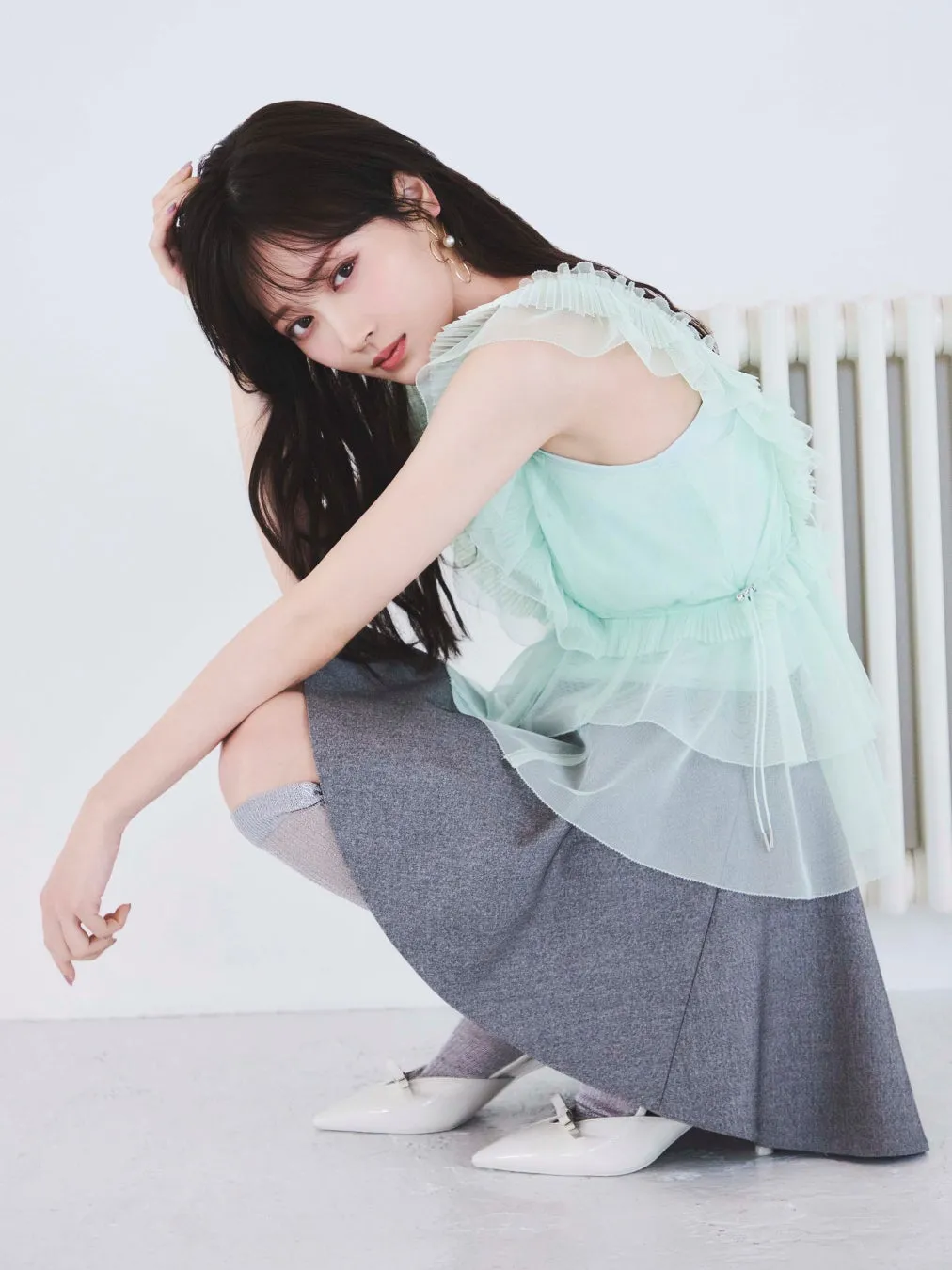 女性がしゃがみこみ、こちらを見ている写真。彼女はミントグリーンのトップス、グレーのスカート、白い靴を履いている。