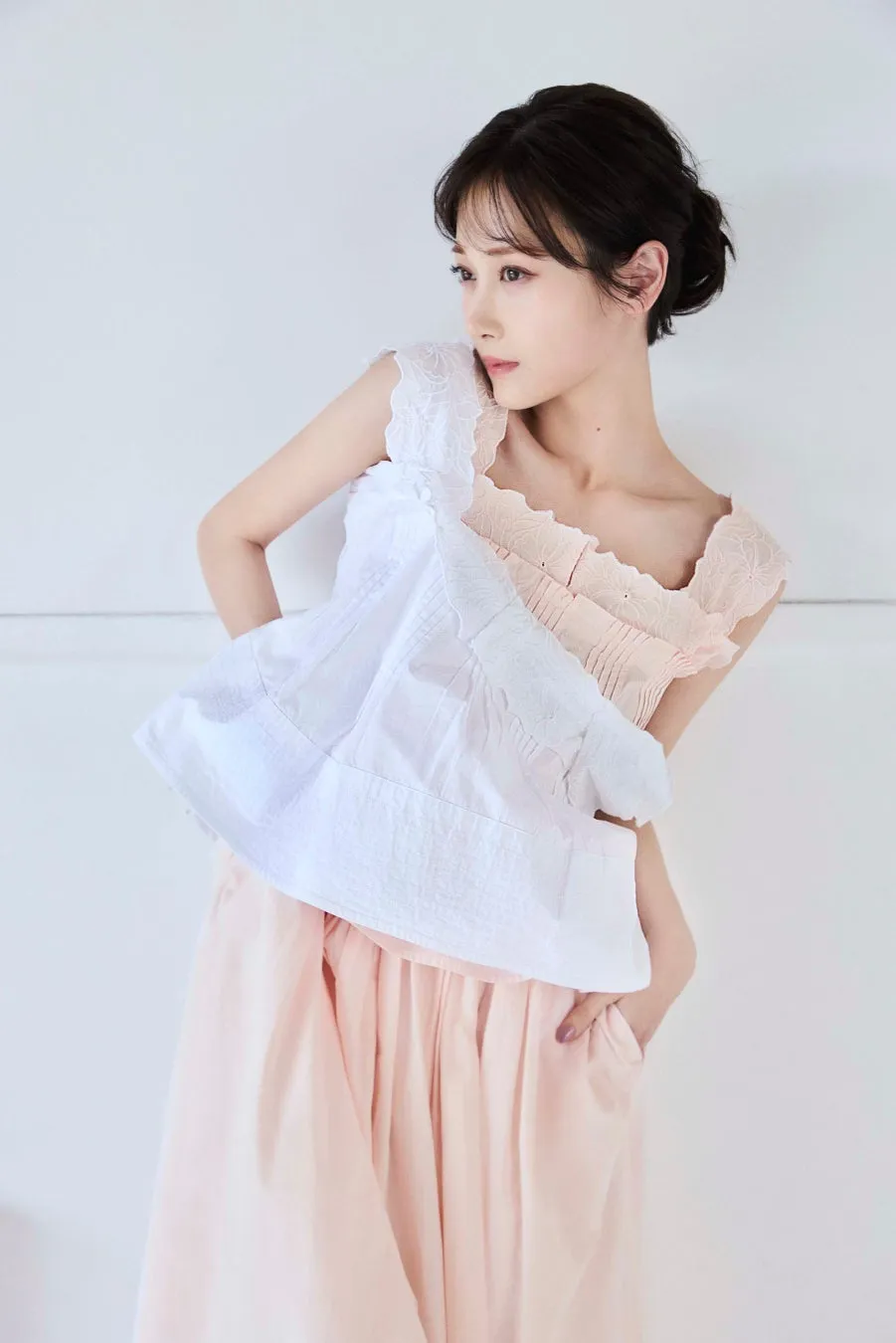 女性が白いトップスとピンクのスカートを着て、片手をポケットに入れている写真です。