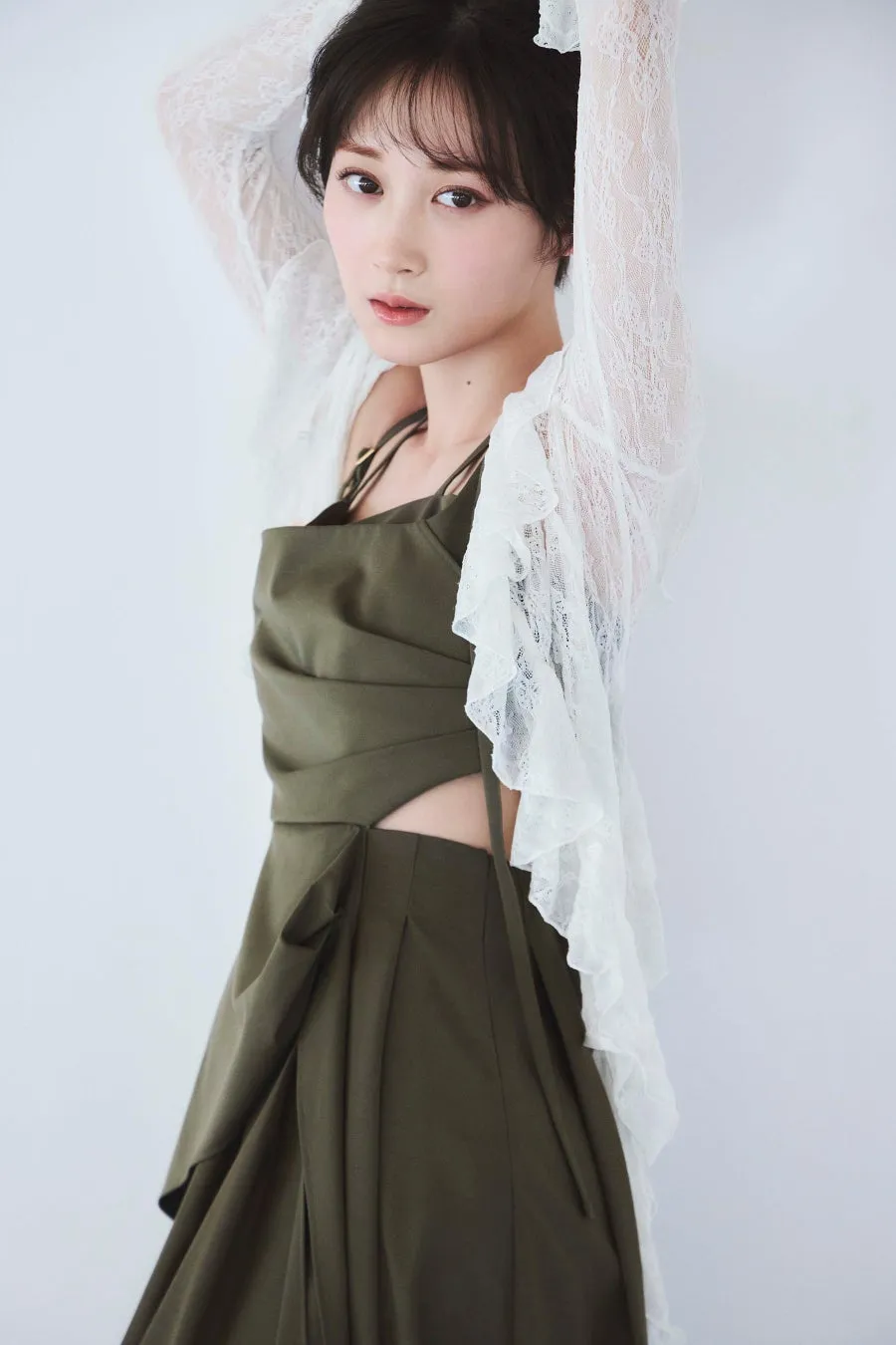 女性が白いレースのトップスとオリーブグリーンのドレスを着て、腕を上げてポーズを取っている写真。