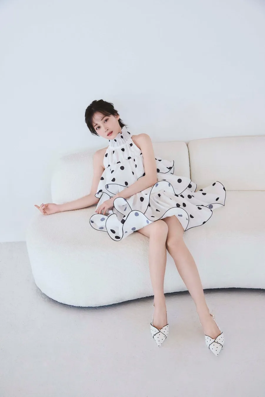 白いソファに座り、水玉模様のドレスを着た女性のポートレート。